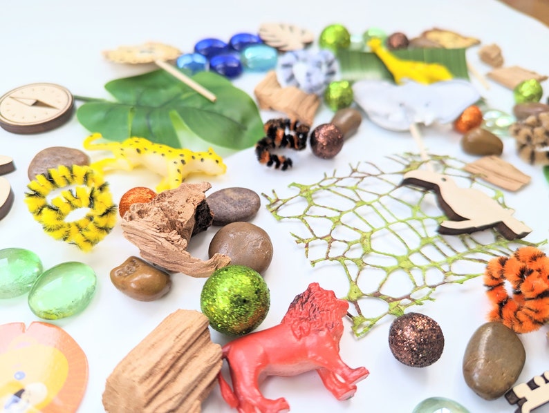 May include: A collection of jungle-themed toys and objects, including a lion, a cheetah, a toucan, a green leaf, a wooden log, a net, and a variety of colorful beads and stones.