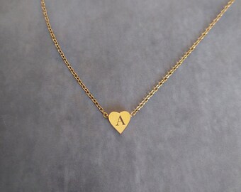 May include: A gold chain necklace with a small heart pendant. The heart has the letter "A" engraved on it.