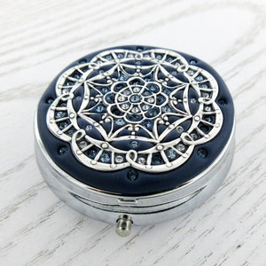 Op de afbeelding: Een ronde, zilveren pillendoos met een blauw emaille deksel. Het deksel heeft een zilveren mandala-ontwerp met heldere en blauwe strass steentjes.