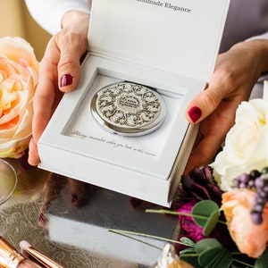 May include: A white box with a silver compact mirror inside. The mirror has an ornate design with a floral pattern. The box has the text "Handmade Elegance" on the top and "Always remember when you look in this mirror" on the inside.