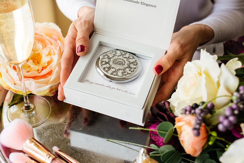 May include: A white box with a silver compact mirror inside. The mirror has an ornate design with a floral pattern. The box has the text "Handmade Elegance" on the top and "Always remember when you look in this mirror" on the inside.
