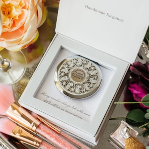 May include: A silver compact mirror with an ornate design and rhinestones. The mirror is in a white box with the words "Handmade Elegance" and "Always remember when you look in this mirror that I will love you forever and ever" printed on it.