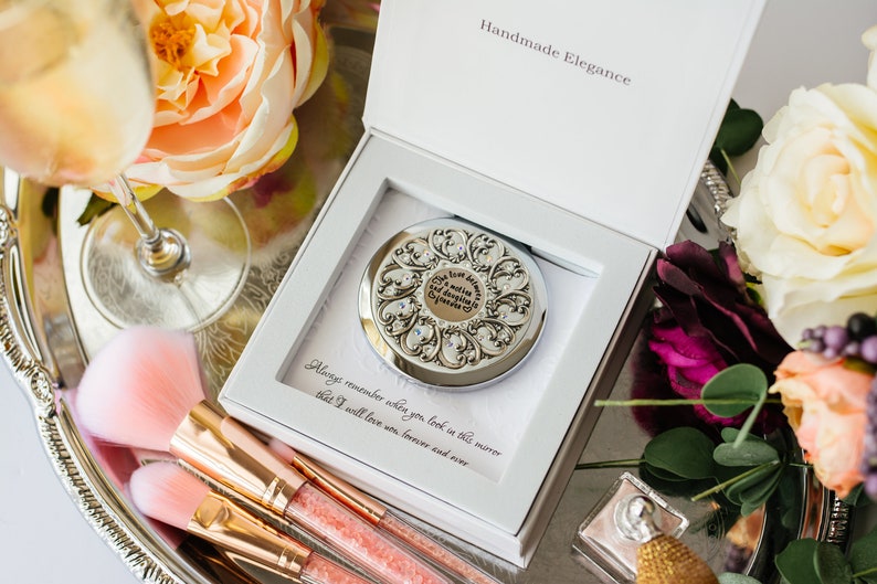 May include: A silver compact mirror with an ornate design and rhinestones. The mirror is in a white box with the words "Handmade Elegance" and "Always remember when you look in this mirror that I will love you forever and ever" printed on it.