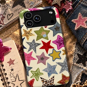 May include: A smartphone case with a cream-colored background featuring a repeating pattern of multi-colored stars. The stars include various textures and designs such as denim, leopard print, glitter, solid red, yellow, green, and pink.