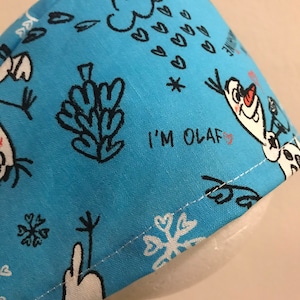 May include: Blue fabric scrub hat with a white and black Olaf print. The hat has a white border and the text "I'm Olaf" in red.