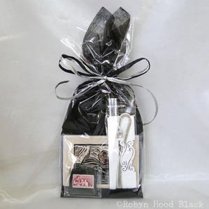 May include: A black gift bag with a clear plastic window, filled with a small white card, a silver key chain, and a silver pen. The bag is tied with a black ribbon.