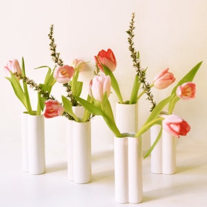 May include: A group of white ceramic vases with a textured surface, each holding a bouquet of pink and white tulips.