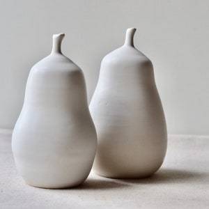 May include: Two white ceramic pear-shaped vases. The vases are smooth and have a matte finish.