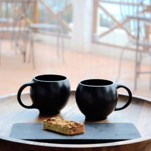 Black stoneware ceramic Eva teacups in smooth high-fired stoneware by Maia Ming Designs, inspired by Eva Zeisel. Tactile, sculptural form for mindful tea rituals and quiet mornings,for tea enthusiasts and design-conscious interiors.