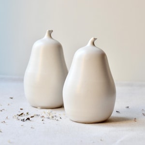 Puede incluir: Dos saleros y pimenteros de cerámica blanca en forma de pera sobre una superficie blanca.