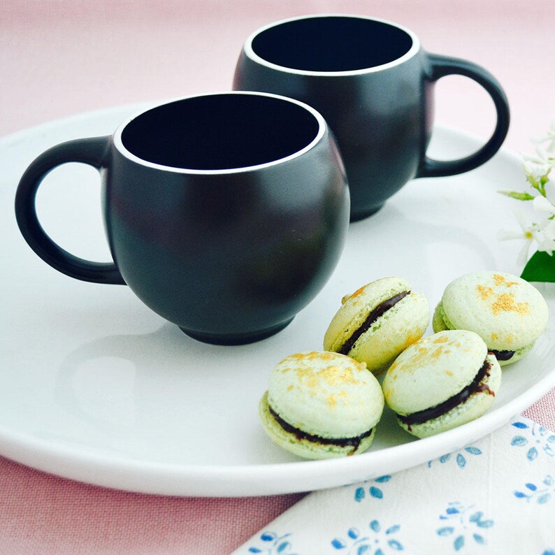 Modern minimalist Eva teacups in black and white stoneware by Maia Ming Designs, inspired by Eva Zeisel, styled with macarons for mindful tea rituals.