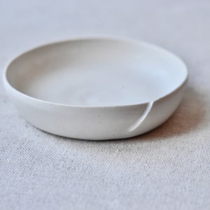 May include: A small, white ceramic bowl with a slightly uneven rim. The bowl is smooth and has a matte finish.