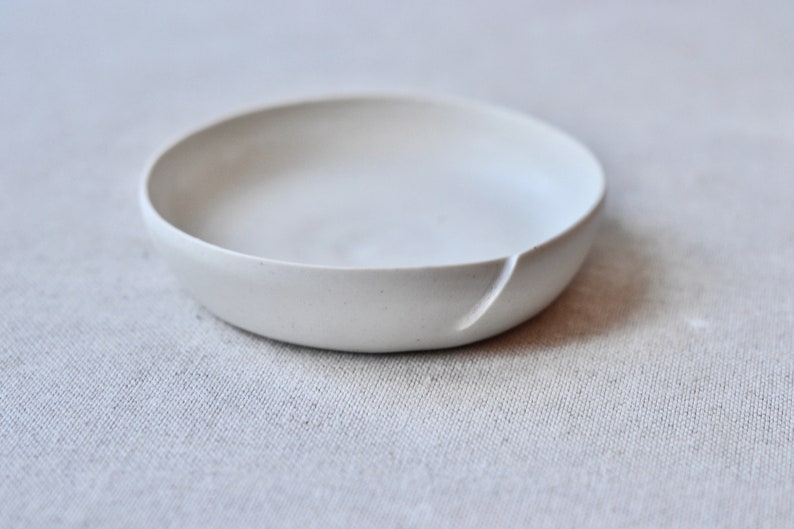 May include: A small, white ceramic bowl with a slightly uneven rim. The bowl is smooth and has a matte finish.