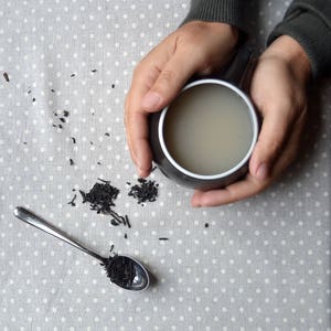 Eva teacup cradled in hands by Maia Ming Designs, inspired by Eva Zeisel. Tactile, sculptural form for mindful tea rituals and quiet mornings, handcrafted  for tea enthusiasts and design-conscious interiors.
