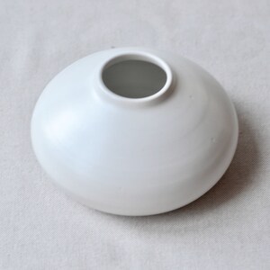 May include: A white ceramic vase with a rounded, bowl-like shape and a wide opening.
