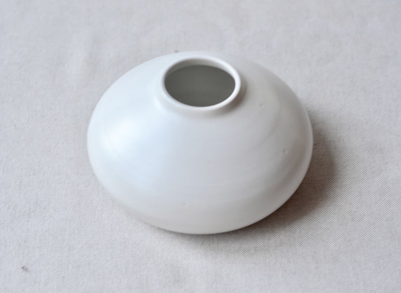 May include: A white ceramic vase with a rounded, bowl-like shape and a wide opening.