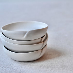 May include: A stack of four white ceramic bowls with a unique, slightly curved rim. The bowls are nested together, creating a visually appealing display.