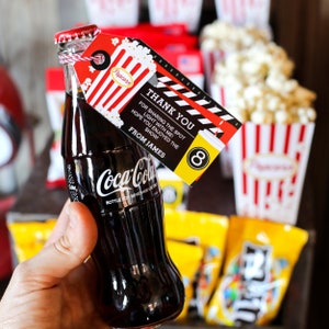 May include: A small glass bottle of Coca-Cola with a red and white striped tag that says "Thank You for sharing the spot light with me! Hope you enjoyed the show! From James". The tag also has a popcorn bucket and a movie clapperboard design.