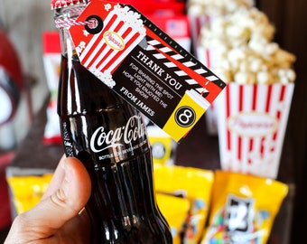 Könnte beinhalten: Eine kleine Glasflasche Coca-Cola mit einem rot-weiß gestreiften Etikett, auf dem steht: "Danke, dass du das Licht mit mir geteilt hast! Ich hoffe, du hast die Show genossen! Von James". Das Etikett hat auch ein Popcorn-Eimer- und ein Filmklappen-Design.