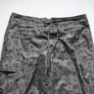 Pu&ograve; includere: Pantaloni cargo grigi con motivo paisley nero. I pantaloni hanno un punto vita con coulisse e una tasca cargo sulla gamba sinistra. Il tessuto ha una leggera lucentezza.