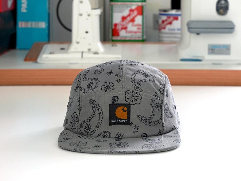 Pu&ograve; includere: Cappellino Carhartt grigio a cinque pannelli con motivo paisley. Il cappellino presenta una toppa quadrata con il logo Carhartt e una 'C' arancione sul davanti. Il cappello &egrave; realizzato in tessuto morbido e ha una visiera piatta.