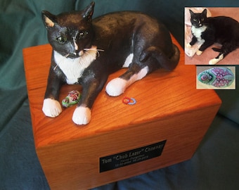 May include: A wooden box with a black and white cat figurine on top. The cat is lying down with its paws outstretched. The box has a black plaque with the text "Tom "Chub Lazer" Conaway" and "Never Forgotten 12-01-2004 04-21-2015".