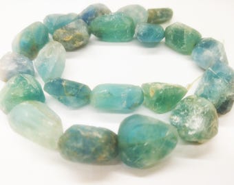 Op de afbeelding: Een streng aquamarijn edelsteen kralen in verschillende tinten blauw en groen. De onregelmatige, getrommelde stenen hebben een natuurlijk uiterlijk. Deze kralen zijn geschikt voor het maken van sieraden.