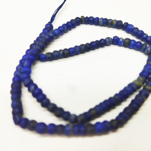 May include: A strand of small, round, dark blue beads with a slightly irregular shape. The beads are strung together on a thin, dark blue string. The beads appear to be made of a stone-like material.