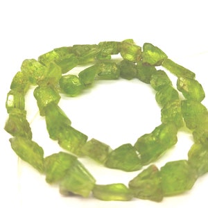 May include: A necklace of rough-cut, light green peridot gemstones. The stones are irregularly shaped and strung together, creating a natural, organic look. The peridot beads are a vibrant, translucent green.