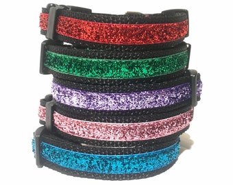May include: Five different colored dog collars with glitter trim. The collars are stacked on top of each other. The colors are red, green, purple, pink, and blue.