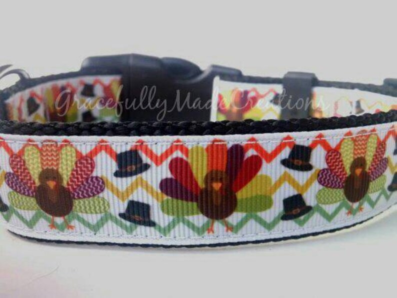 May include: A white and black dog collar with a Thanksgiving turkey pattern. The collar features a repeating pattern of turkeys wearing pilgrim hats and a chevron design.