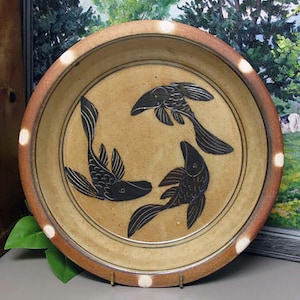 May include: A ceramic plate with a brown rim and white dots. The plate features three black fish designs.