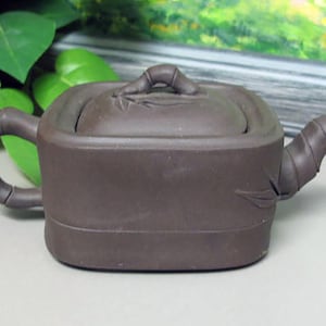 May include: A brown ceramic teapot with a square body and a bamboo-shaped handle and spout. The lid has a bamboo design and a raised handle.
