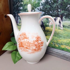 May include: White ceramic pitcher with a lid and handle, featuring an orange pastoral scene. The pitcher has a curved spout and a red trim. A decorative piece for serving beverages.