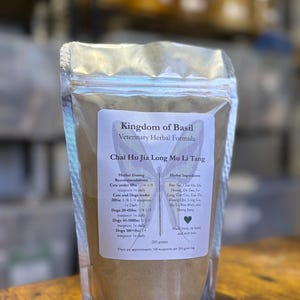 May include: A silver resealable pouch containing a brown herbal powder labeled "Kingdom of Basil Veterinary Herbal Formula Chai Hu Jia Long Mu Li Tang". The label includes a list of herbal ingredients and dosing recommendations for cats and dogs.
