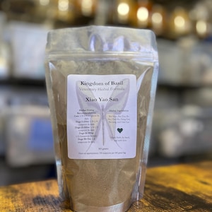 May include: A resealable pouch of brown powder labeled "Kingdom of Basil Veterinary Herbal Formula Xiao Yao San". The label includes a list of herbal ingredients and dosing recommendations for cats and dogs.