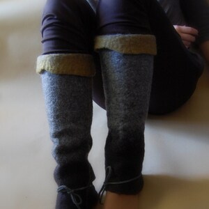 May include: A pair of gray and black leg warmers with brown leather ties. The leg warmers are made of a soft, fuzzy material and have a subtle ombre effect.