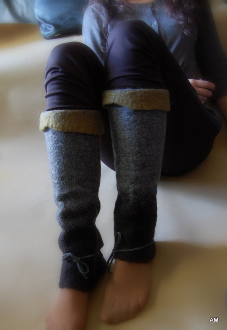 May include: A pair of gray and black leg warmers with brown leather ties. The leg warmers are made of a soft, fuzzy material and have a subtle ombre effect.
