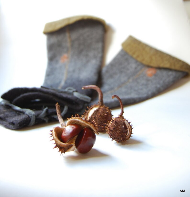 May include: Three brown horse chestnut conkers with prickly husks, two with the husks open and one closed, on a white surface next to two gray wool socks with brown cuffs.
