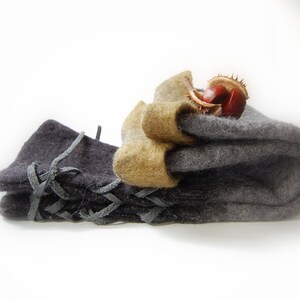 May include: Two pairs of felted wool fingerless gloves. One pair is gray and the other is black with leather lacing. The gray pair has a brown chestnut on top.
