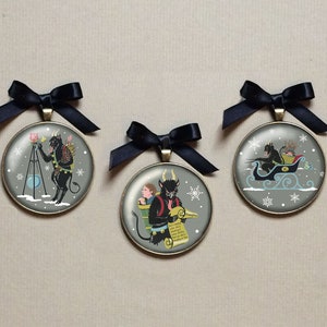 May include: Three round Christmas ornaments with a black and white illustration of a devil figure. The first ornament shows the devil holding a horn and standing on a tripod. The second ornament shows the devil carrying a child on his back. The third ornament shows the devil riding in a sleigh.