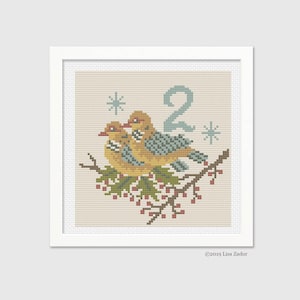 May include: A framed cross-stitch featuring two yellow and blue birds perched on a branch with red berries. The number "2" and two snowflakes are above the birds. The artwork is in a white frame.