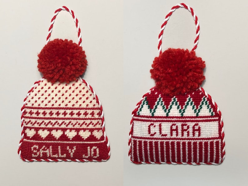 May include: Two red and white knit stocking cap ornaments with pom-poms. One ornament says "Sally Jo" and the other says "Clara".