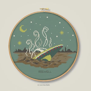 May include: A cross-stitch pattern of a UFO crashed in a field at night. The UFO is green and yellow with red lights. The field is brown and there are stars in the sky. The text "ROSWELL" is below the UFO.