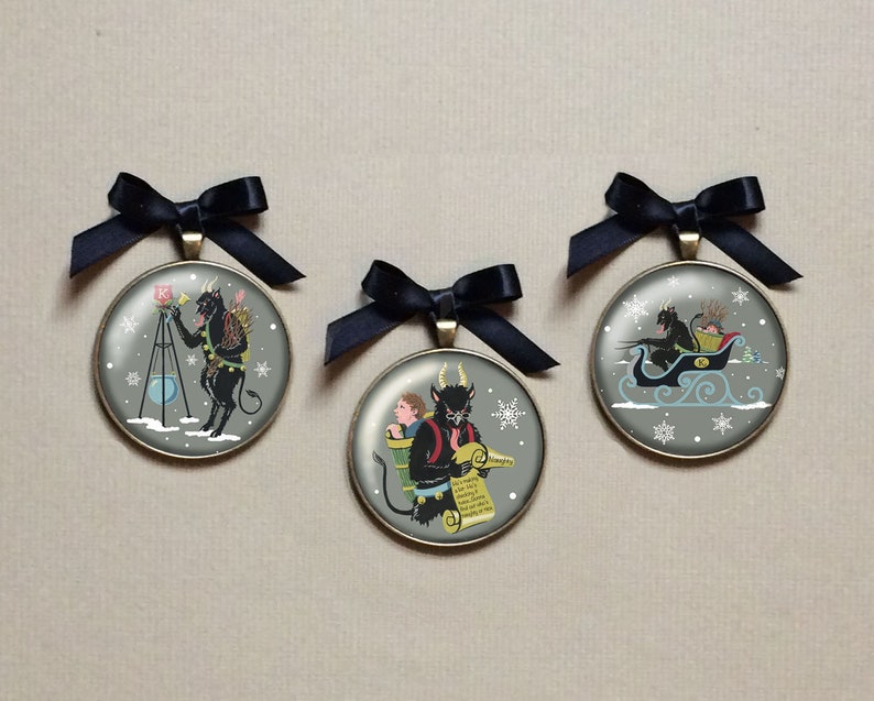 May include: Three round Christmas ornaments with a black and white illustration of a devil figure. The first ornament shows the devil holding a horn and standing on a tripod. The second ornament shows the devil carrying a child on his back. The third ornament shows the devil riding in a sleigh.