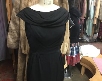 May include: A black sleeveless dress with a cowl neck and a fitted silhouette. The dress is on a mannequin with the label "Royal Form" visible.