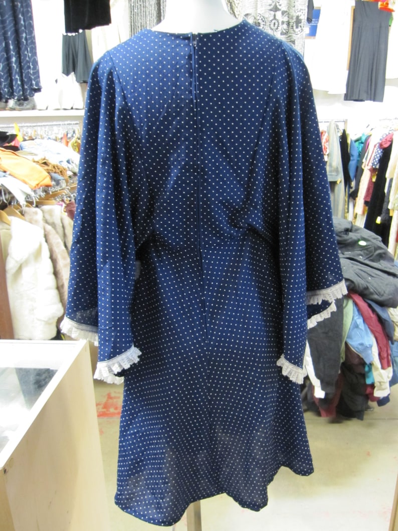 May include: A navy blue dress with white polka dots and white lace trim on the sleeves. The dress has a long, flowing skirt and a fitted bodice.