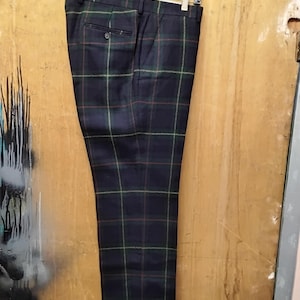 May include: Navy blue plaid trousers hanging on a black hanger. The trousers feature a classic plaid pattern in green, red, and yellow lines over a navy background. The pants have a buttoned back pocket and a button closure.