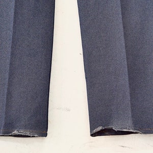 May include: Close-up of the bottom hems of a pair of dark blue denim pants. The hems are frayed and uneven.