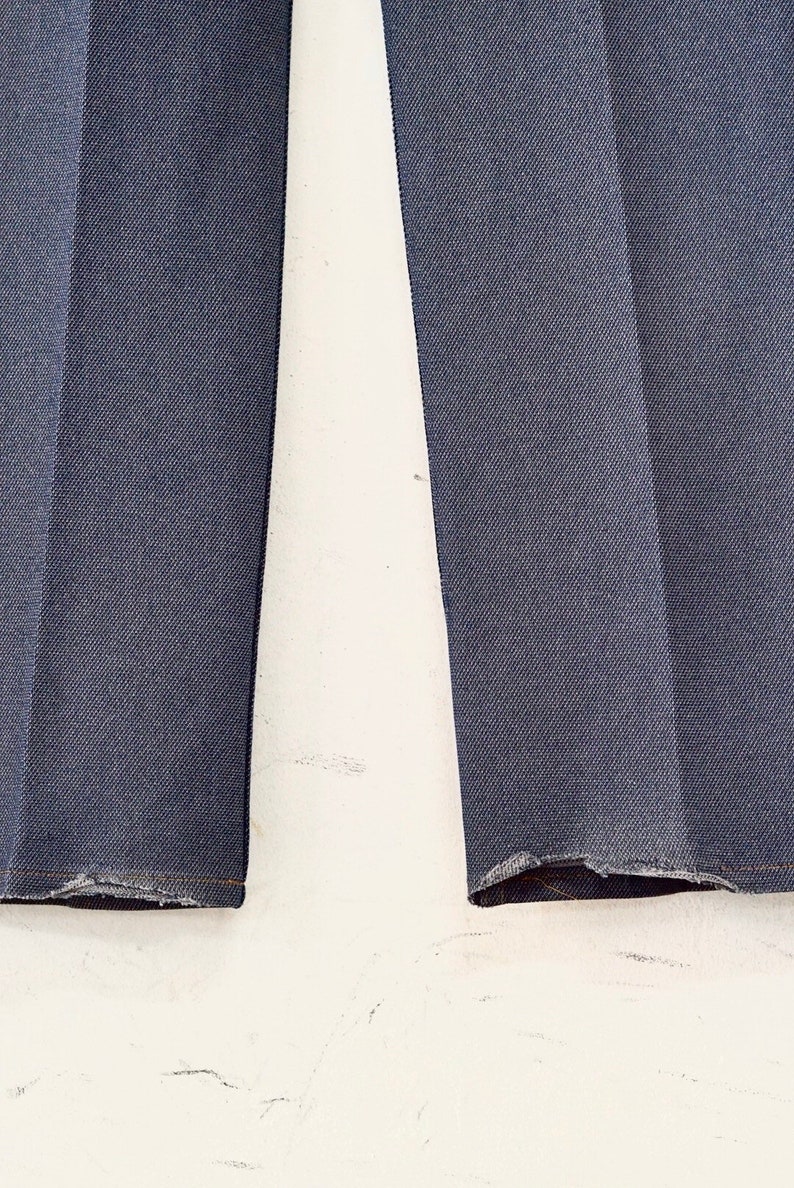 May include: Close-up of the bottom hems of a pair of dark blue denim pants. The hems are frayed and uneven.